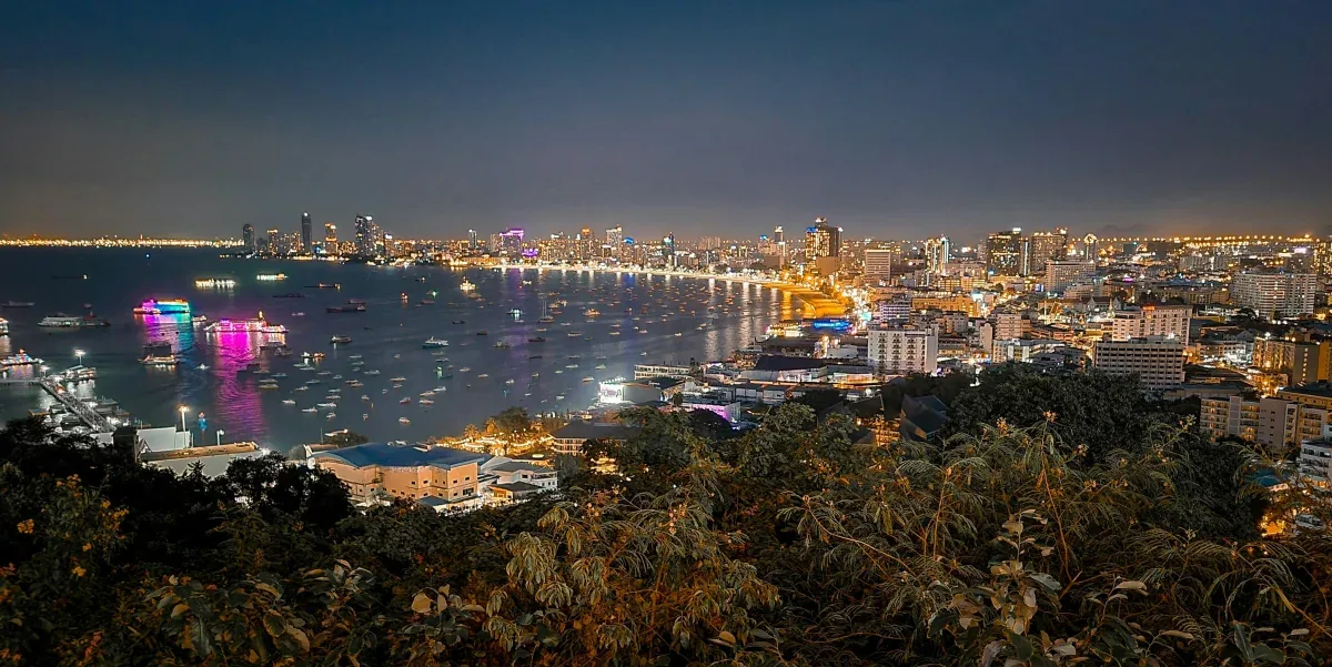 Panoramic night view of Pattaya Bay with illuminated city skyline, waterfront lights reflecting on water, and boats in the bay